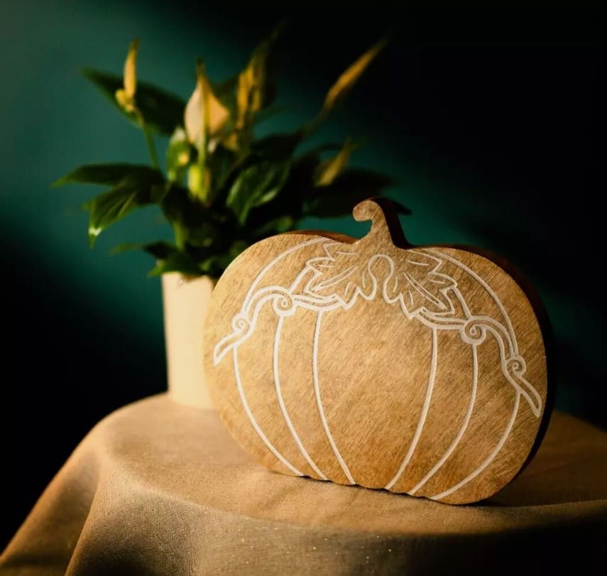 Pumpkin wooden cheeseboard sitting on a table with green background on table