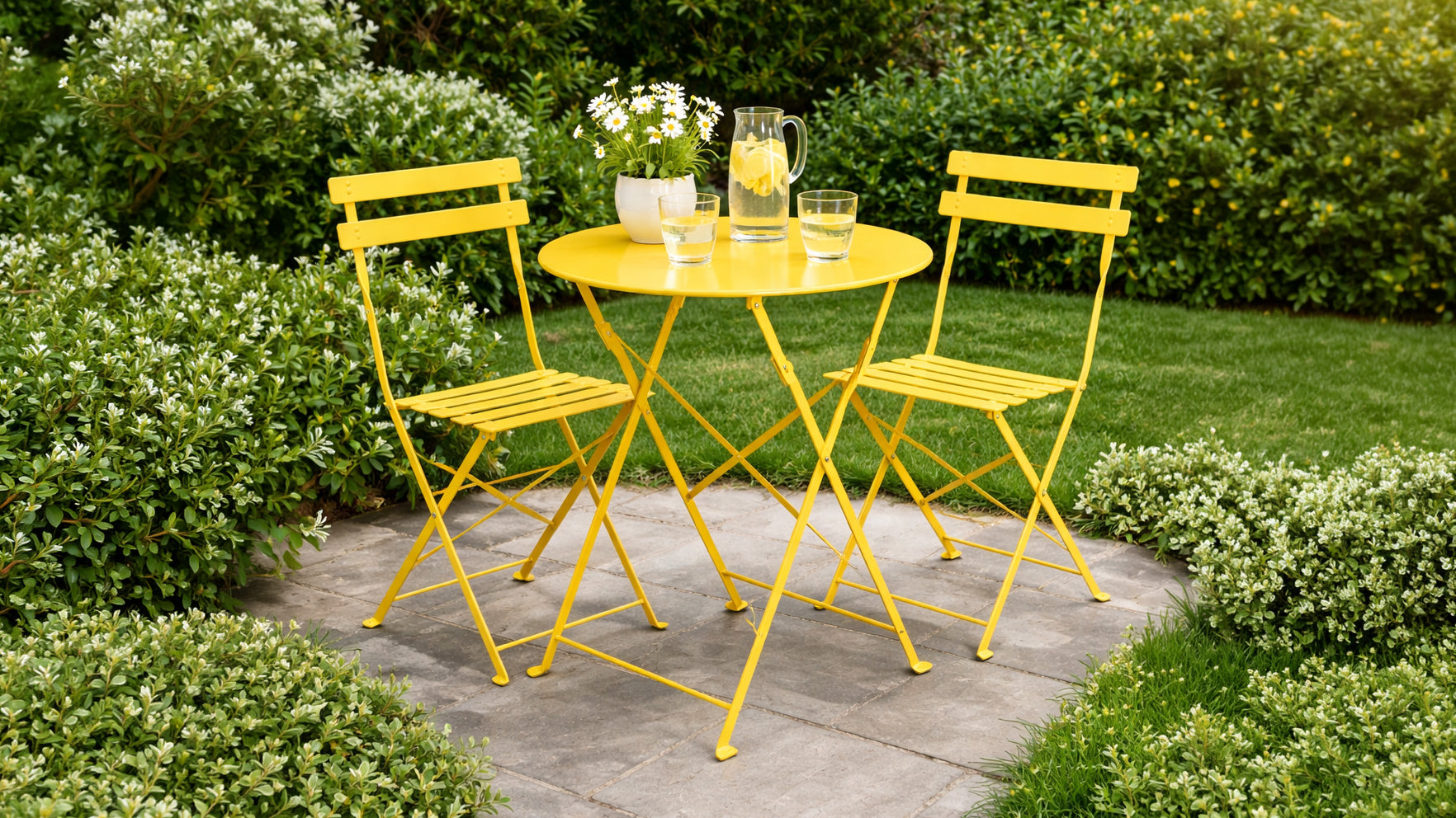A bright yellow three-piece metal patio bistro set consisting of a round table and two folding chairs, styled on a gray stone patio with green garden foliage in the background.