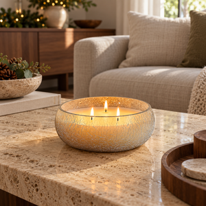 Three-wick crackle-effect glass candle glowing on a travertine coffee table beside a cream sofa.