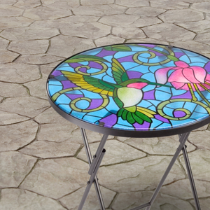 Colorful stained glass table with a hummingbird design on a stone patio.