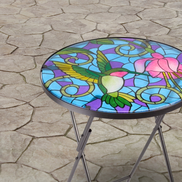 Colorful stained glass table with a hummingbird design on a stone patio.
