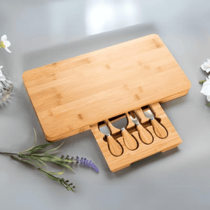 Wooden cheese board set with four knives on a light gray surface with flowers.