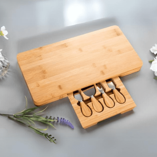 Wooden cheese board set with four knives on a light gray surface with flowers.