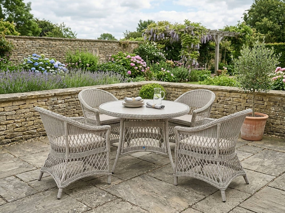 Outdoor patio set with a round table and four chairs on a stone patio, surrounded by a garden.