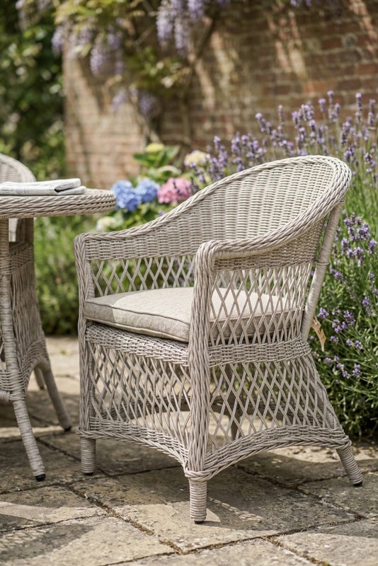 Outdoor patio set with a round table and four chairs on a stone patio, surrounded by a garden.