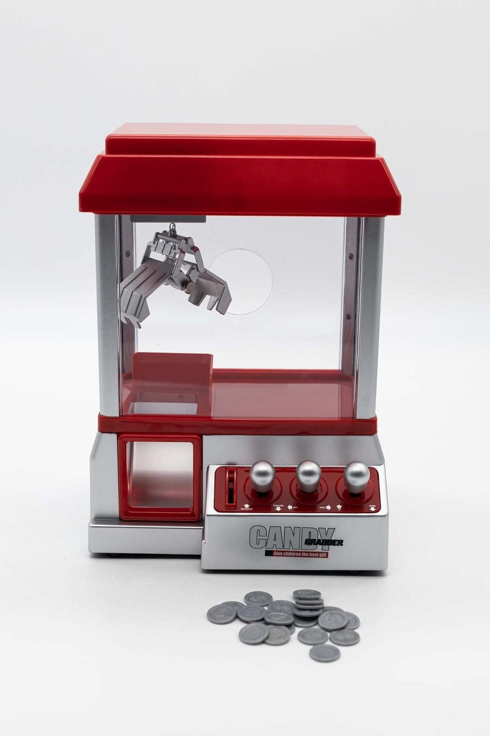 A small red and silver candy grabber machine designed for arcade-style gameplay, placed on a wooden table.