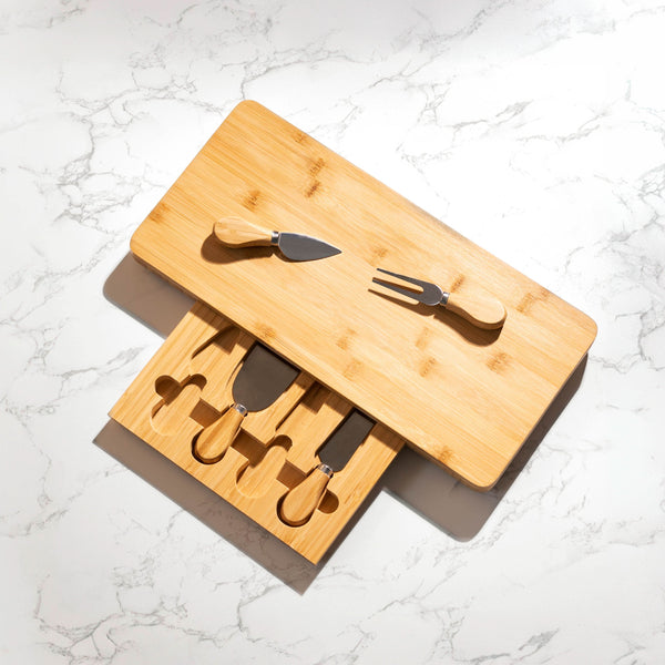 Bamboo cutting board with knives, forks, and spoons on a marble surface