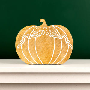 Wooden pumpkin decoration with white carving on a shelf against a green wall