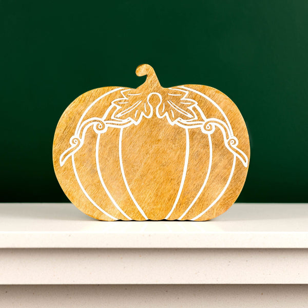 Wooden pumpkin decoration with white carving on a shelf against a green wall