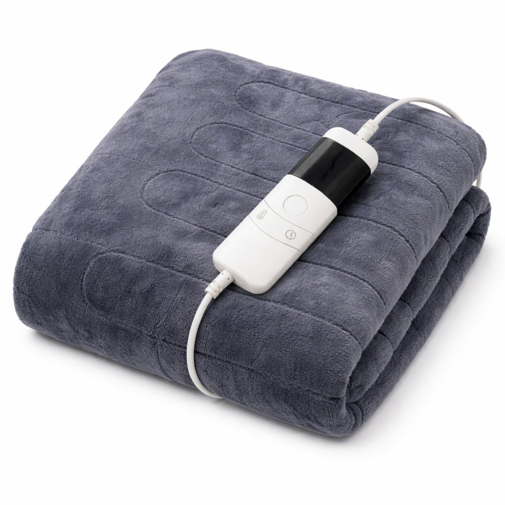 A woman reclining on a beige couch under a dark gray plush blanket, holding a white mug and using a white remote control with a temperature display.