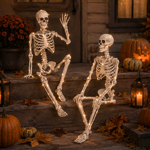 Two decorative skeletons with warm white LED lights sit on rustic wooden steps in a Halloween-themed outdoor setting with pumpkins, autumn leaves, and lanterns.