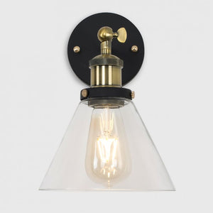 Wall-mounted light fixture with clear glass shade and brass fitting on a white background