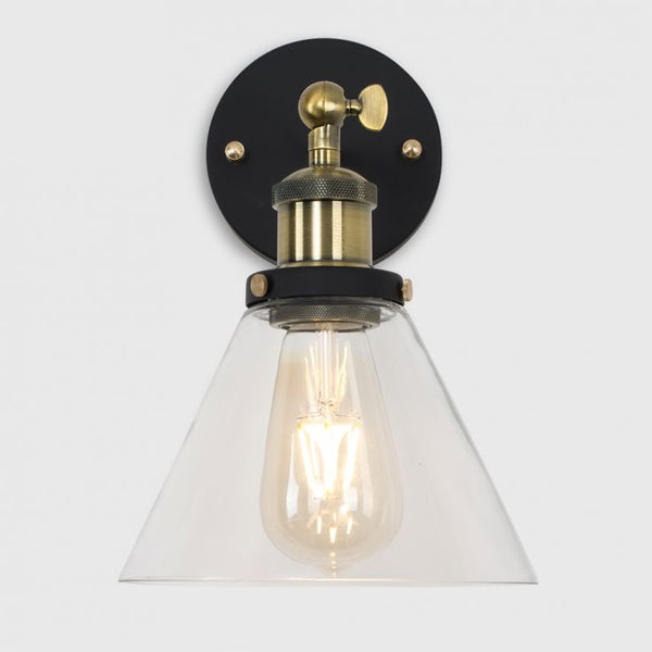 Wall-mounted light fixture with clear glass shade and brass fitting on a white background