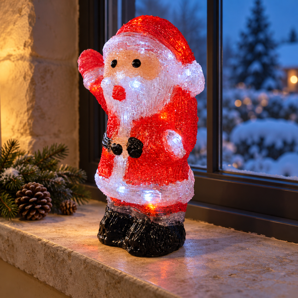 A glittery Santa Claus figurine with built-in LED lights, standing on a stone windowsill with a snowy outdoor view and pinecones in the background.