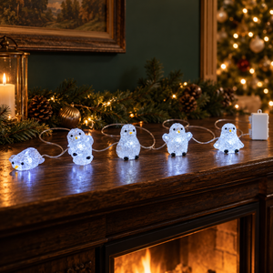 Five glowing penguin-shaped string lights arranged across a dark wooden mantel
