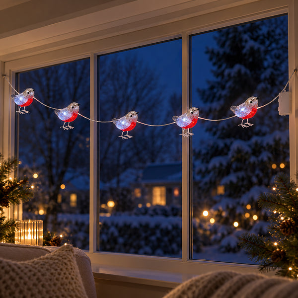 Christmas string lights shaped like robins, with glowing silver bodies and bright red bellies hung across a large window