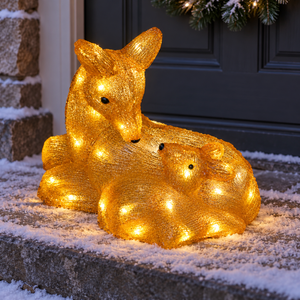 a golden glowing deer and baby deer figurine with warm white LED lights displayed outdoors in a snowy scene