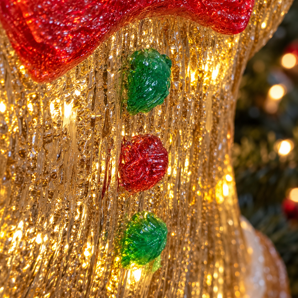 Close-up of a glittery gold Christmas stocking ornament with a red textured top and three vertical red and green button details, lit with warm golden lights.
