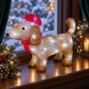 Illuminated acrylic dachshund wearing a red Santa hat and scarf on a windowsill with cool white LEDs and festive lights behind