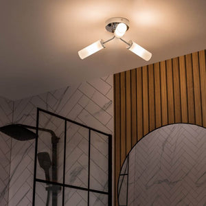 Modern ceiling light fixture in a bathroom with tiled walls and wooden panel.