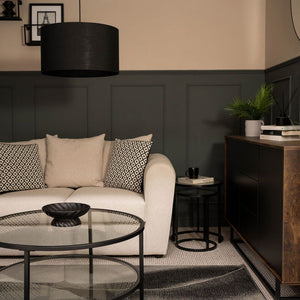 Modern living room with a beige sofa, round glass coffee table, and dark wood sideboard.