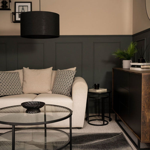 Modern living room with a beige sofa, round glass coffee table, and dark wood sideboard.
