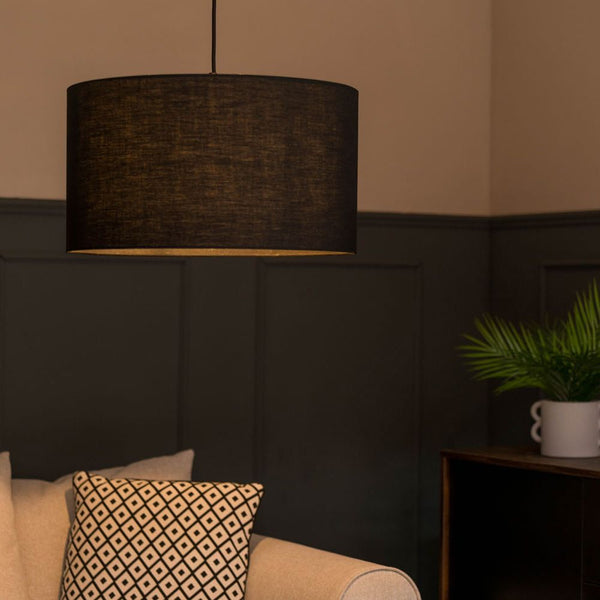 Dark lampshade hanging above a sofa with decorative pillows in a dimly lit room.