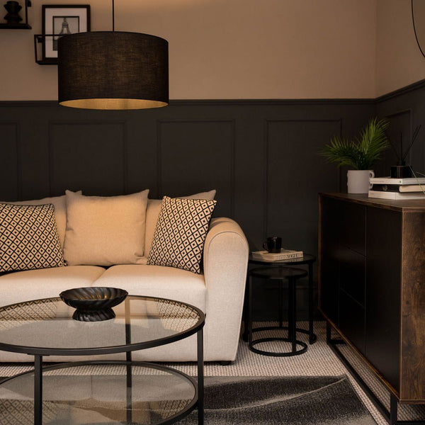 Modern living room with a beige sofa, round glass coffee table, and dark wall paneling.