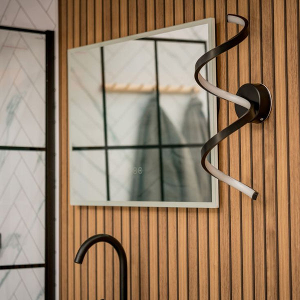 Modern wall-mounted light fixture on a wooden wall with a mirror and faucet in the background.