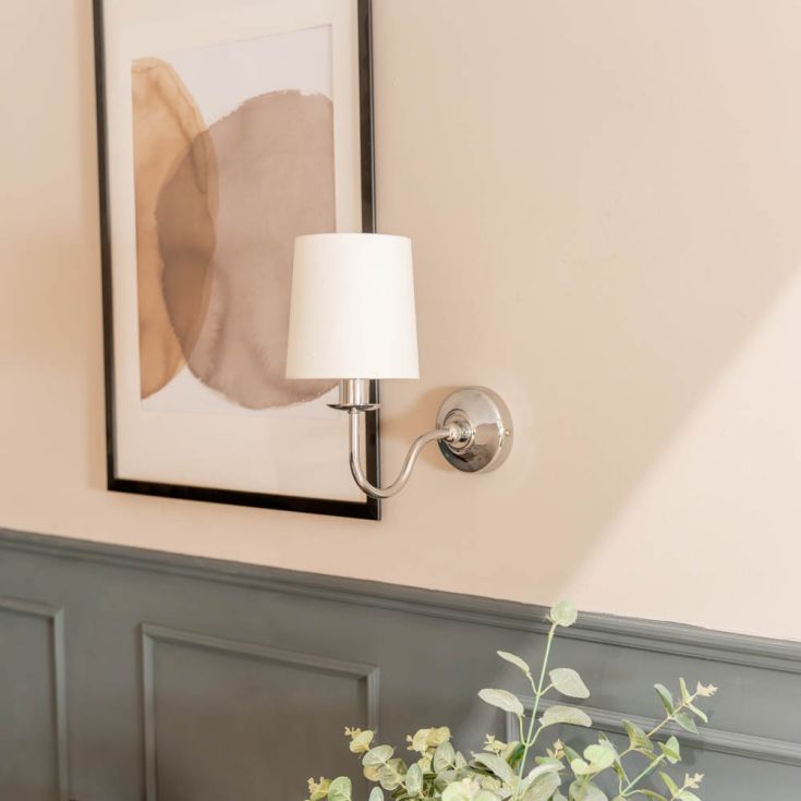 Wall-mounted lamp with a white shade on a beige wall above a gray panelled wall.