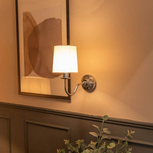 Wall-mounted lamp with a white shade on a wall with a framed abstract painting.