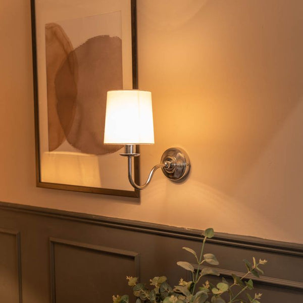 Wall-mounted lamp with a white shade on a wall with a framed abstract painting.