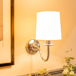 Wall-mounted lamp with white shade and gold fixture on a yellow wall.