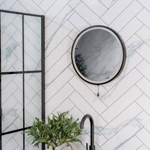 Round mirror on a tiled wall with a plant and faucet in the foreground