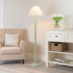 Green floor lamp in a living room setting with a beige armchair and white side table.