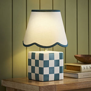 Table lamp with checkered base and scalloped white shade on a wooden surface.
