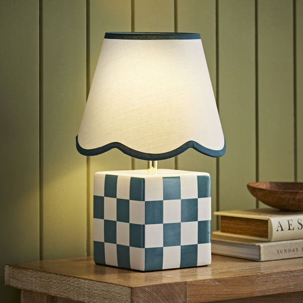 Table lamp with checkered base and scalloped white shade on a wooden surface.