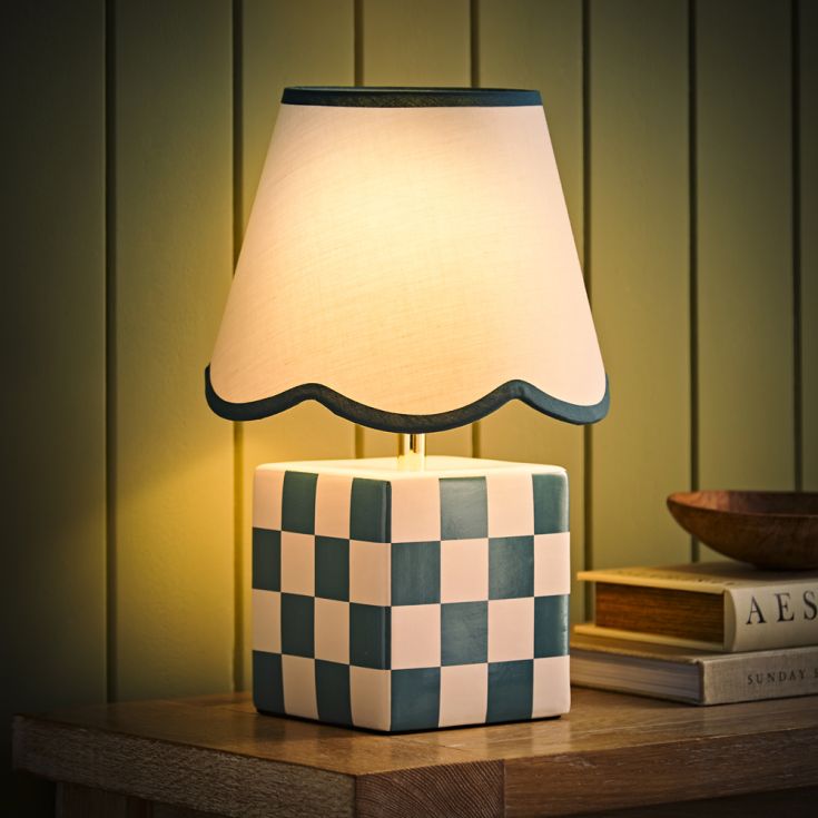 Table lamp with checkered base and scalloped white shade on a wooden surface.