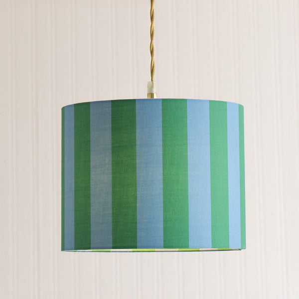Striped green and blue lampshade hanging against a beige wall.