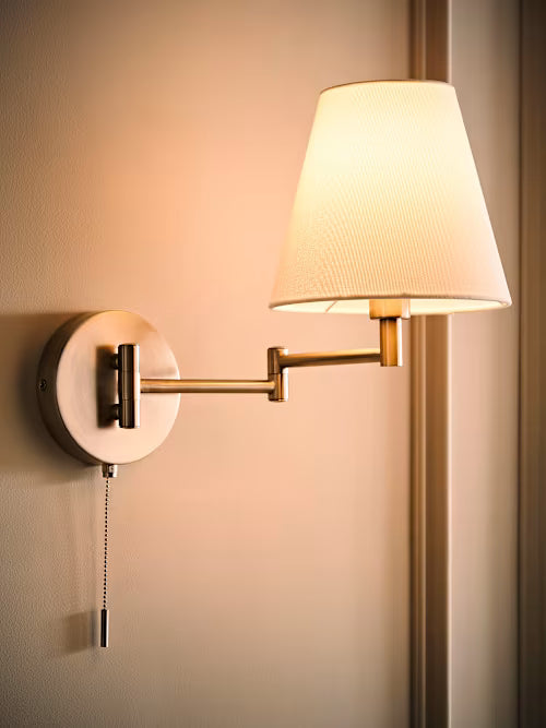 Wall-mounted lamp with a white shade and gold arm on a beige wall.