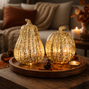 Two glittery gold decorative pumpkins with ribbed textures, lit from within, displayed on a round wooden tray in a cozy living room setting.