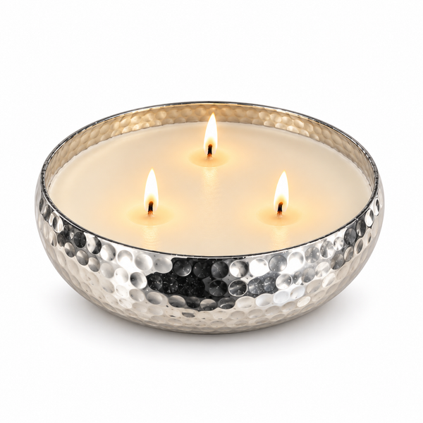 A hammered silver metal candle bowl filled with white wax and three wicks, placed on a white background.