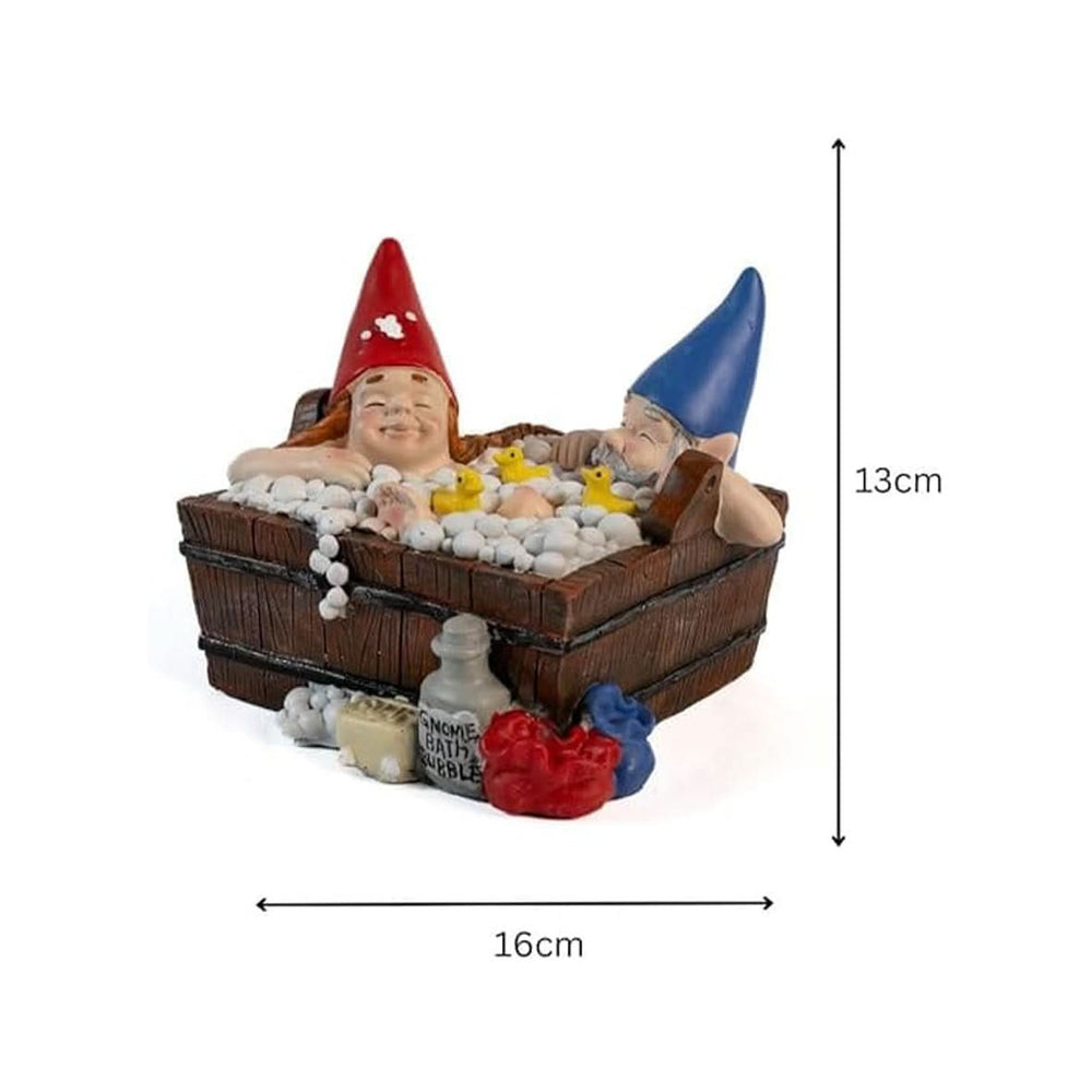 A solar-powered gnome garden ornament sitting in a bathtub, with a red and a blue gnome figurine inside, surrounded by white artificial foam pieces, placed on a grassy surface.