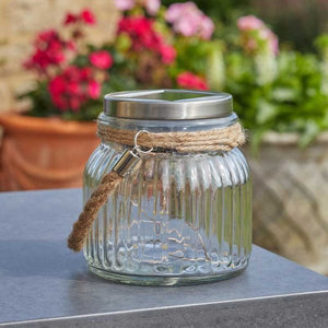 Glass jar with solar light on a table with flowers in the background