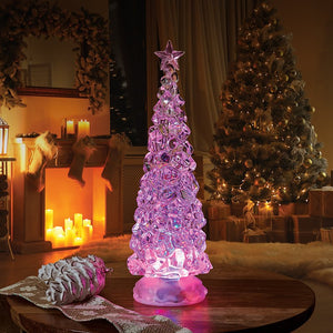 Ice effect LED Christmas tree with a star topper glowing pink on a wooden table beside a festive fireplace.