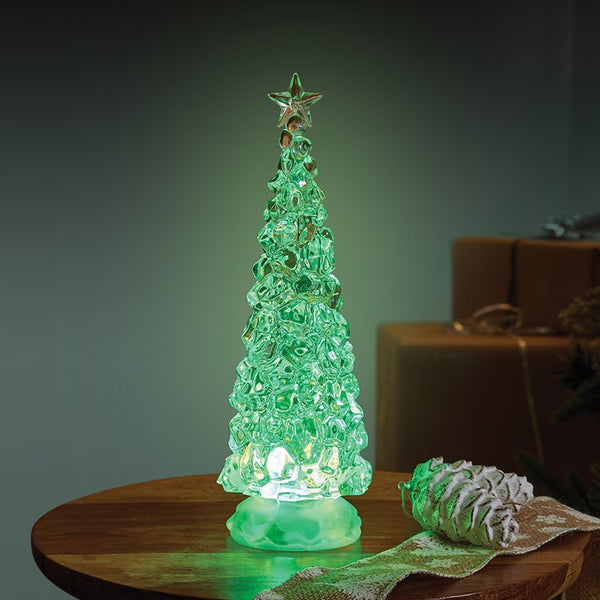 Ice effect LED Christmas tree with a star topper glowing green on a wooden table beside a frosted pine cone and wrapped gifts.