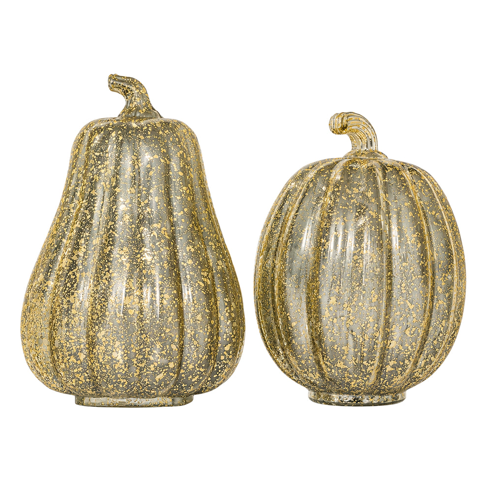 Two decorative glass pumpkins with warm white LED lights inside, one pear-shaped and one round, displayed on a wooden table in a cozy living room setting.