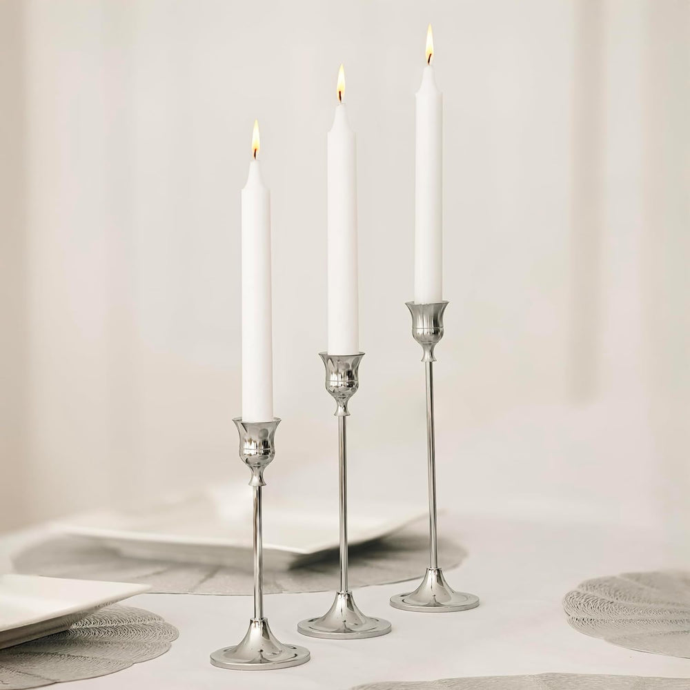 Three silver candlestick holders with white taper candles