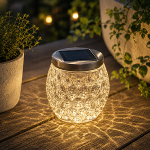 Solar-powered glass lantern emitting a warm glow on a wooden surface with plants in the background.