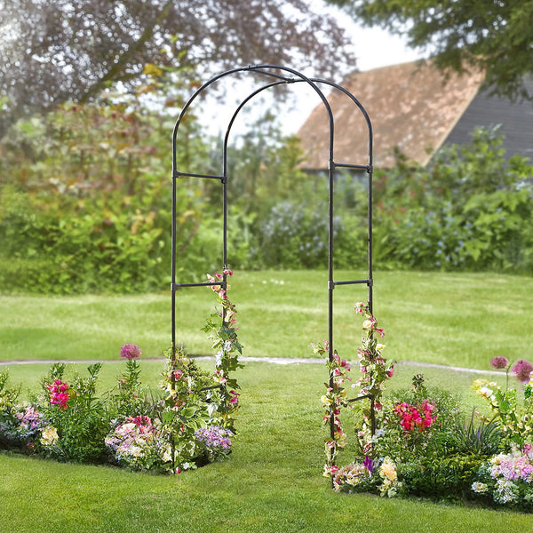 Metal garden arch with floral decorations in a lush garden setting.